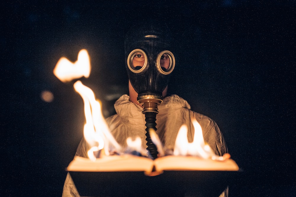 Book Banning - person in a gas mask holds an open book that is on fire